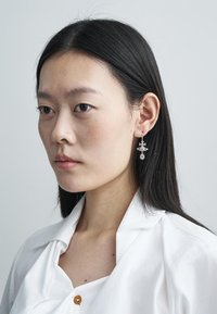 Hõbe tähekujulised kõrvarõngad keerukate detailidega, rippuvad lihtsate konksude küljes, kandsid mudel valget särki, millel on nööbikas. 