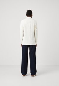 Blazer blanco entallado de manga larga, combinado con pantalones de pierna ancha en color navy. Textura de tela suave, líneas limpias y un diseño minimalista.