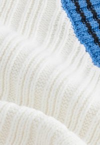 Stricktextil mit geripptem weißen Stoff und einem horizontalen blauen Streifen sowie schwarzen Details. Weiche Textur und nahtloses Design.