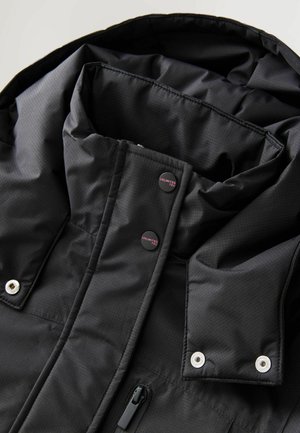 Veste isolée noire avec un col haut, des boutons-pression, une fermeture éclair à l'avant et des accessoires en métal argenté. Présente une texture de tissu à motif.