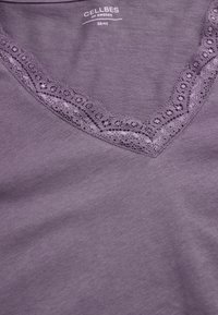 V-kaulustoppi purppuranvärisessä, jossa on hieno pitsireuna kauluksessa. Valmistettu pehmeästä kankaasta, jossa on sileä rakenne. Kokolapussa ilmoitetaan koko 38/40.