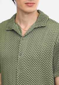Korte mouw shirt in olijfgroen, textuur met een 3D-wafelpatroon, voorzien van een puntige kraag en knoopsluiting. Glad stof.
