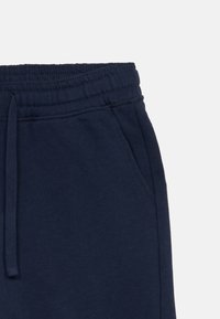 Marineblaue Baumwoll-Sweatpants mit einem elastischen Bündchen, einem Kordelzug und seitlichen Taschen. Glatte Textur mit verstärkten Nähten.