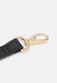 La sangle en cuir noir présente une surface texturée et une boucle en métal doré avec un détail de marque, conçue pour fixer les objets en toute sécurité.