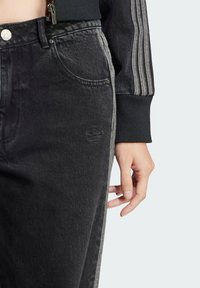 Schwarze Denim-Jeans verfügen über eine distressed Textur mit einem dezenten geprägten Logo. Sie haben graue Seitenstreifen und ein klassisches Fünf-Taschen-Design.