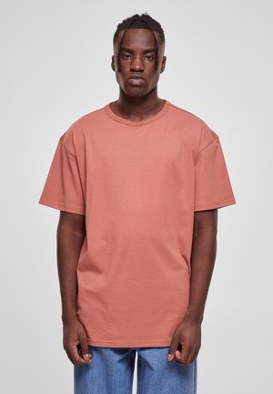 Camiseta de corte holgado y mangas cortas en tela de algodón coral, con cuello redondo y dobladillo recto. Se combina con pantalones de mezclilla azul claro.