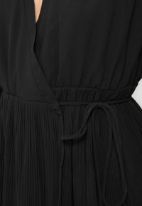 Μαύρο φόρεμα με ντεκολτέ σε σχήμα V και πλισέ φούστα. Διαθέτει ελαστική μέση με υφασμάτινη ζώνη που δένει. Κατασκευασμένο από ελαφρύ, απαλό υλικό.