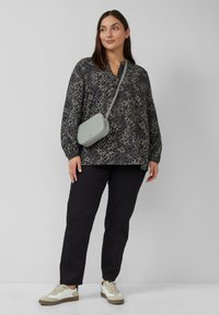 Grijze leoprint blouse met een losse pasvorm, gecombineerd met zwarte broek en beige sneakers. Een kleine grijze schoudertas voegt detail toe.