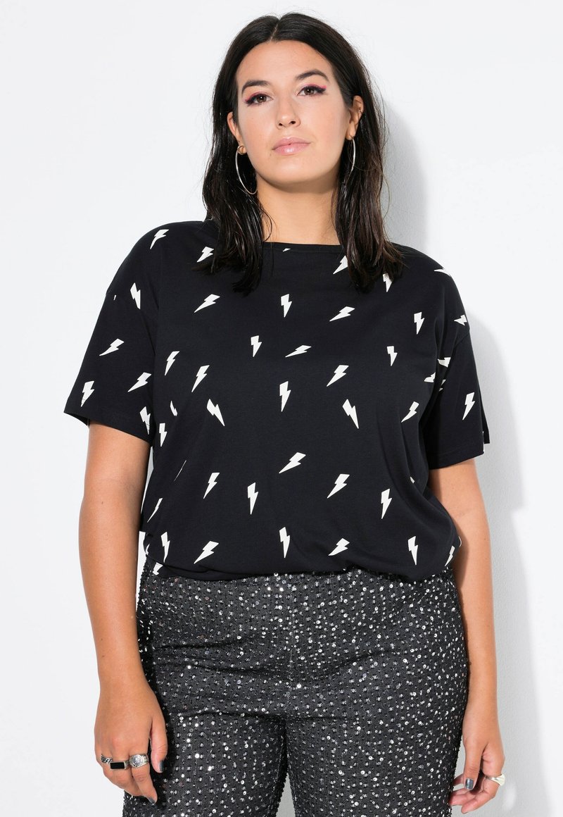 Czarny t-shirt z krótkim rękawem z powtarzającym się białym wzorem błyskawic, w połączeniu z błyszczącymi czarnymi spodniami z cekinami.