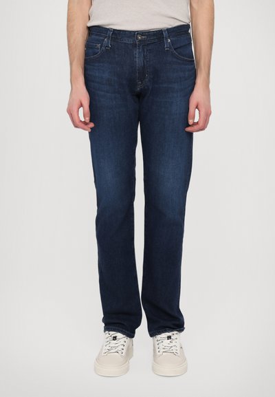 Dunkelblaue Jeans aus Denim mit geradem Bein, Fünf-Taschen-Design und Knopfverschluss. Getragen mit weißen Sneakern.