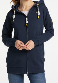Marinblå zip-up huvtröja med dragsko, som har vita och gula snörakenter, kengurufickor samt ribbade ärmslut och nederkant.