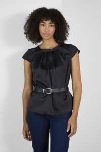 Haut noir en satin à manches courtes avec un col plissé, cintré à la taille par une ceinture noire avec une boucle en or, associé à un jean foncé.