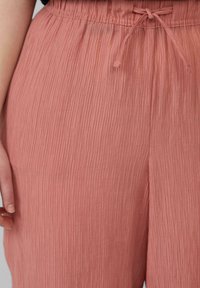 Pantalons en tissu pêché doux et froissé avec une taille élastique et un cordon de serrage. Texture légère et coupe décontractée.