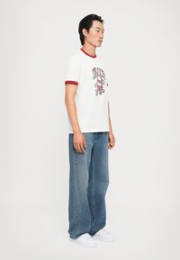 Hvid bomulds t-shirt med rød ribbet krave og korte ærmer, med et trykt "MILANO" grafik, parret med løse blå denim jeans og hvide sneakers.