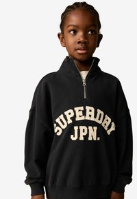 Svart sweatshirt med hög krage och kvartzip, med stor off-white text "SUPERDAY JPN." på framsidan och ribbade ärmslut.
