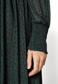 Vestido de estampado animal em verde com punhos franzidos; textura suave e tecido leve, apresentando um corte solto e mangas longas.