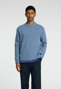 Hellblauer Pullover mit Rundhalsausschnitt und gerippten Bündchen, kombiniert mit dunklen Hosen. Weiche Textur mit lockerer Passform.