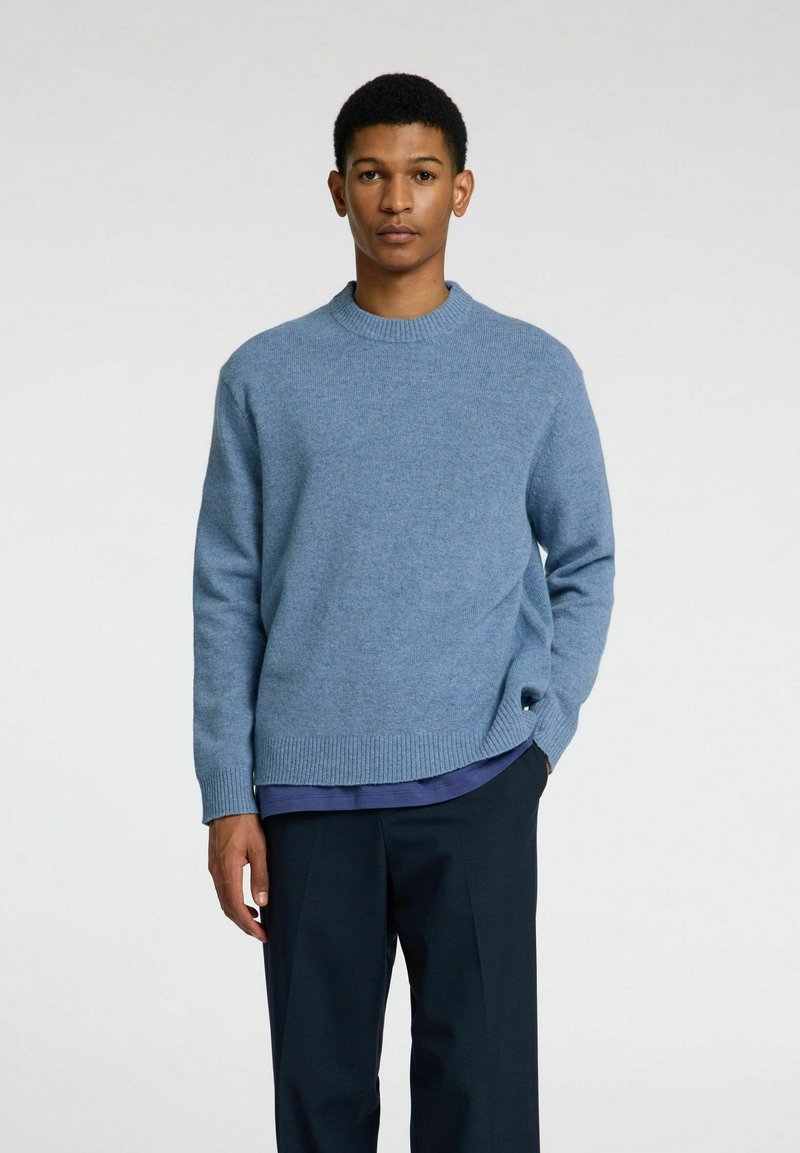 Hellblauer Pullover mit Rundhalsausschnitt und gerippten Bündchen, kombiniert mit dunklen Hosen. Weiche Textur mit lockerer Passform.