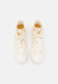 Høje sneakers lavet af hvidt lærred med et gult blomstermønster. Har hvide snørebånd og en tekstureret gummisål.