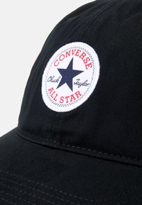 Must musta, millel on kaarjas ääreosa. Esiküljel on valge ümmargune plaaster musta tähega ja punase tekstiga, mis ütleb "CONVERSE ALL STAR."