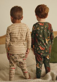 Deux enfants vêtus de pyjamas : l'un en haut rayé beige et pantalon à motifs, l'autre en vert foncé avec des imprimés d'animaux colorés.