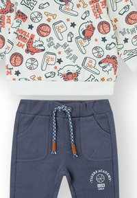 Sudadera con base blanca y estampados deportivos coloridos. Pantalones jogger de algodón azul marino con dos bolsillos y cordón con diseño.