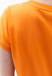 Oranžové tričko s krátkým rukávem vyrobené z měkké bavlny, s kulatým výstřihem a malými žebrovanými detaily na rukávech a límci.