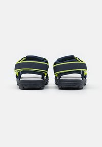 Mørkeblå sandaler med reflekterende gule detaljer, justerbare stropper og teksturerte gummisåler. Designet for holdbarhet og komfort.