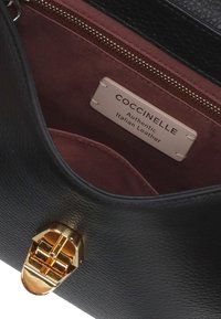 Borsa a mano in pelle nera con chiusura in metallo dorato e interno in tessuto bordeaux con etichetta che riporta la dicitura "Coccinelle - Pelle Italiana Autentica."