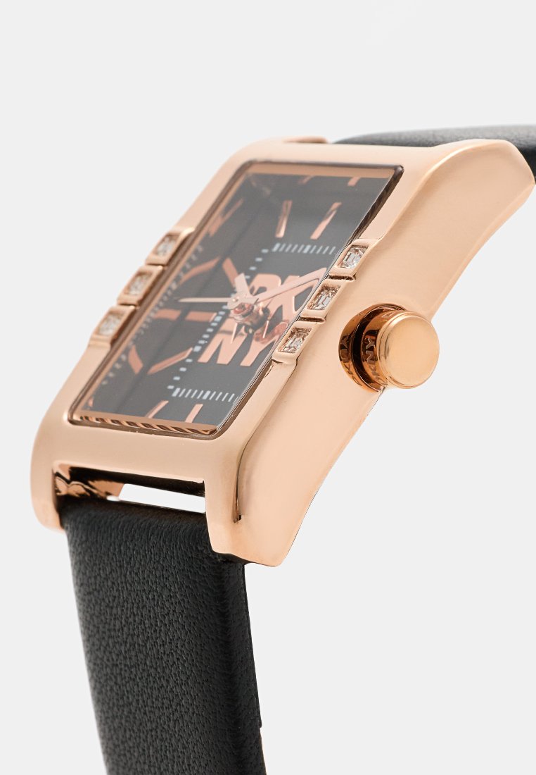 Orologio rettangolare con tonalità rosa dorata, quadrante nero, cinturino in pelle e dettagli in cristallo sulla lunetta. Presenta una corona prominente per le regolazioni.