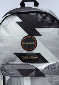 Grafische rugzak met een zwart-wit geometrisch patroon en een gestructureerde afwerking, ronde logopatch en rechthoekig merklabel.
