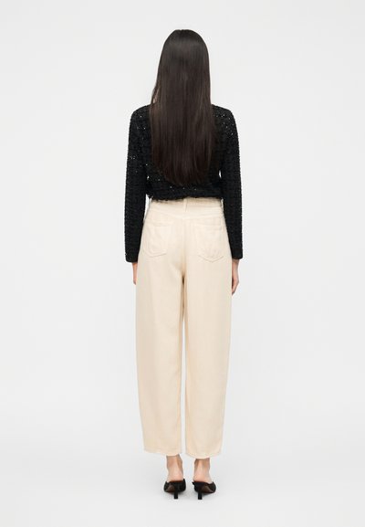 Μαύρο μακρυμάνικο τοπ με υφή, συνδυασμένο με μπεζ παντελόνι ψηλόμεσο, φαρδύ. Το μοντέλο φοράει μαύρα ψηλοτάκουνα mules.