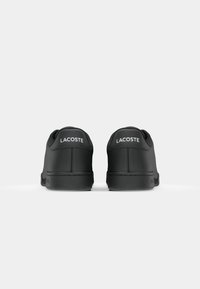 Baskets Lacoste noires en cuir lisse, avec un bout rond et un logo blanc sur le talon. Design minimaliste avec des semelles plates.