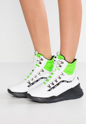 Baskets montantes blanches et vert néon avec semelles épaisses noires et logo MSGM noir portées sur jambes nues sur fond uni.