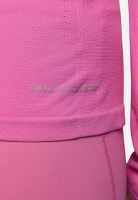 Top sportivo rosa con tessuto testurizzato e orlo a coste. Logo "DRI-FIT" in grigio chiaro vicino al fondo. Design liscio e aderente.