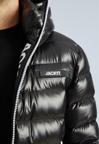 Geacă puffer neagră cu un finisaj lucios, fermoar pe față și glugă. Prezintă un etichetă proeminentă "JACK1T" pe pieptul stâng.