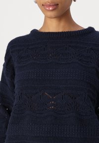 Maglione lavorato a maglia blu navy con un design testurizzato caratterizzato da motivi a traforato, scollo rotondo e polsini a coste.