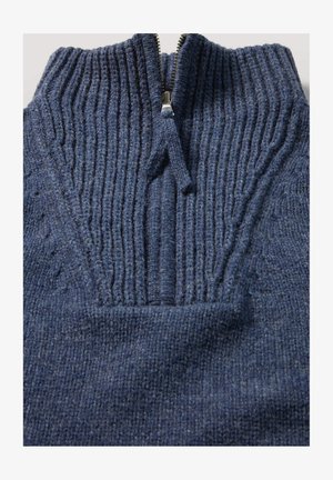 Marineblauwe gebreide trui met een geribbelde structuur, rits tot de helft van de kraag en opvallende stiksels door de stof heen.