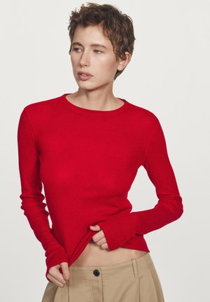 Czerwony longsleeve z okrągłym dekoltem, dopasowany krój i ściągacze, zestawiony z beżowymi spodniami. Gładka faktura na całej powierzchni.