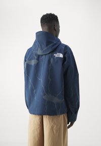 Námořnická modrá bunda s texturovaným, vzorovým designem, vybavená kapucí a logem The North Face na horní části zad.