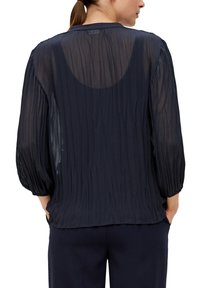 Diepblauwe, doorschijnende blouse met een gerimpelde textuur, opbollende lange mouwen en een ronde halslijn. De achterkant heeft een subtiele ovale uitsnede.