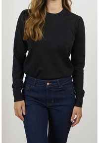 Maglione nero a maglia con scollatura e polsini a coste, abbinato a jeans blu scuro con cuciture a contrasto e chiusura frontale con bottone.