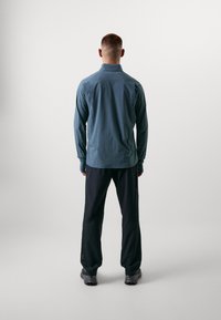 Lichtgewicht herenoverhemd met lange mouwen in het blauw, gecombineerd met donkere broeken. Beide hebben een slanke pasvorm en een minimaal ontwerp. Het schoeisel is grijs met getextureerde zolen.
