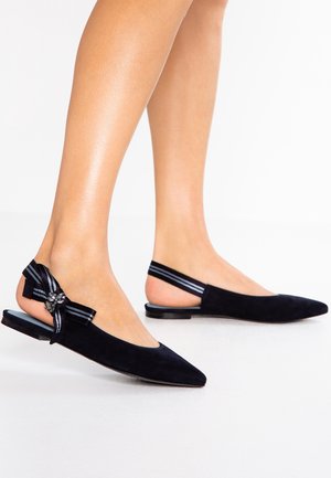 Ballerine slingback nere con punta a punta, con cinturini a righe e fiocco decorativo con gioielli sul lato, indossate a piedi nudi.