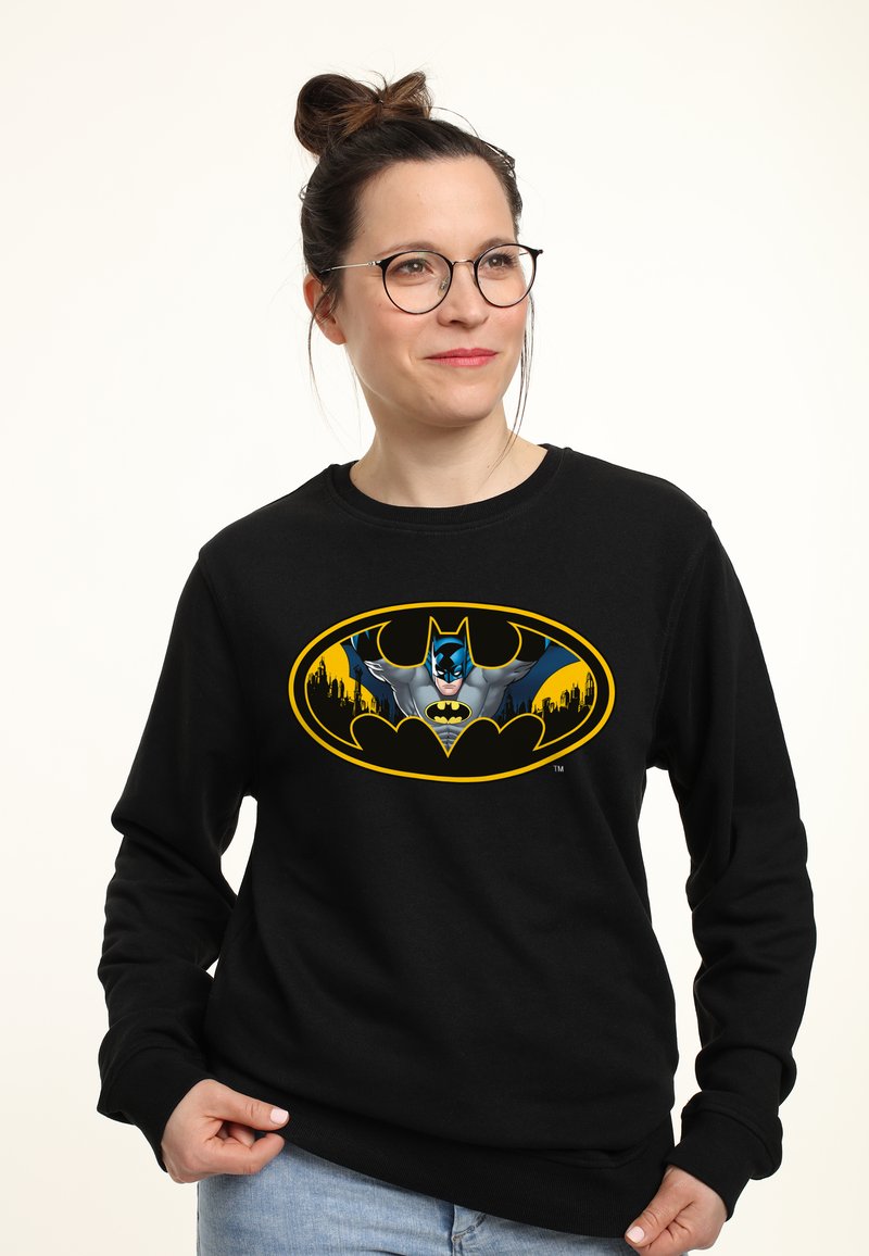 Felpa nera con un grande logo di Batman giallo e grigio accompagnato da un'illustrazione del personaggio. Il tessuto sembra morbido, con collo a giro e maniche lunghe.