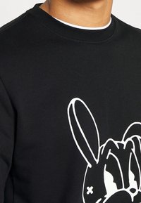 Felpa nera con un grande design di un coniglio in stile cartone animato bianco sulla parte anteriore. Tessuto a trama con scollatura a girocollo a coste.