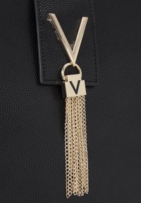 Sac noir texturé avec un accent matériel en forme de V en ton doré, orné d'un charme de serrure et de pampilles en chaîne dorée qui se déversent.