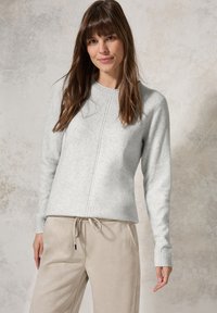 Pull en tricot gris clair avec un col rond, des poignets côtelés et des coutures contrastantes, associé à un pantalon beige à cordon de serrage.