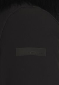 Top sportivo nero con una texture liscia e finitura opaca, dotato di una piccola toppa rettangolare con logo sulla spalla.