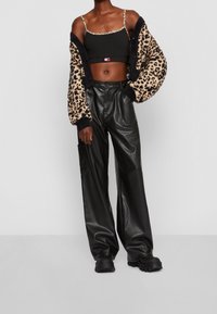 Top noir court avec des bretelles en imprimé léopard, cardigan oversized en imprimé léopard, et pantalon en cuir noir à jambes larges, complété par des bottes noires épaisses.